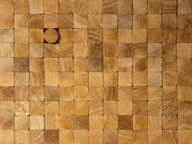 Many square wood blocks stacked up with one different round block within the square block background, standing out from the crowd. Concept image of individuality, going against the grain, standing out from the crowd etc.