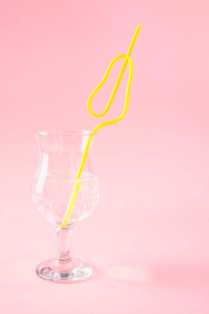 yellow plastic pear shaped cocktail straw in glass on pink background. Concept holiday