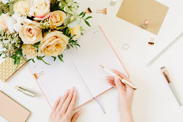 istock woman keeps a diary and planning a day on stylish desktop. Female hand write in pink notebook. Women blog concept with pink notebook and golden watch. Flat lay style. 1221747516