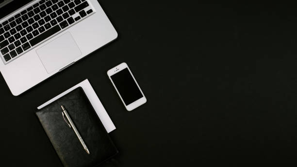 Modern minimalistick workspace with laptop, black leather notebook, smartphone and pen on the black desk