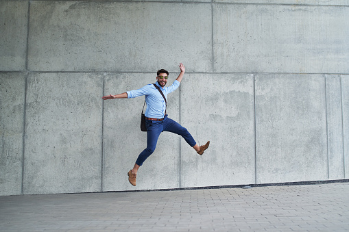 Young businessman jumping in joy and looking at camera outdoors in the city