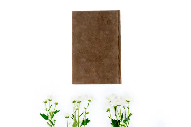 Flat layout of jasmine flowers and a vintage brown book, isolated in white background