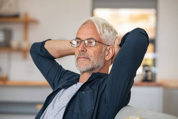 Senior handsome man enjoy the retirement Senior man relaxing at home and thinking with hands behind head. Mature man wearing eyeglasses while resting at home and looking away. Retired old man sitting on couch, thinking about the future. 60 64 years stock pictures, royalty-free photos & images