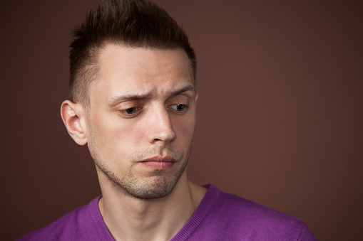 studio close-up portrait of a young man with short hair in a purple sweater on a brown background
