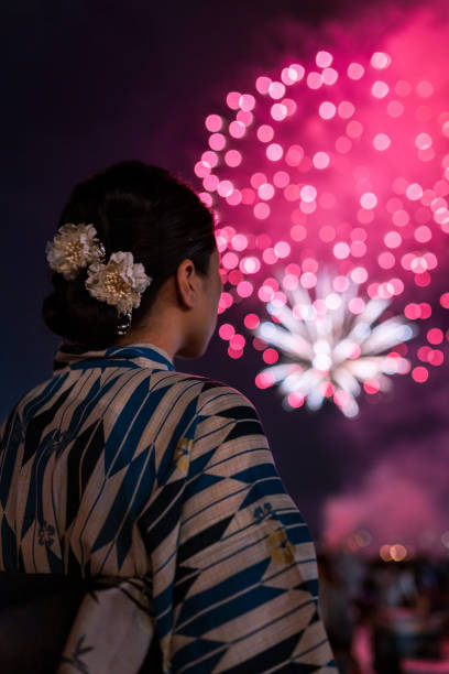 istock Beautiful woman wearing a kimono looking up at fireworks 1221763280