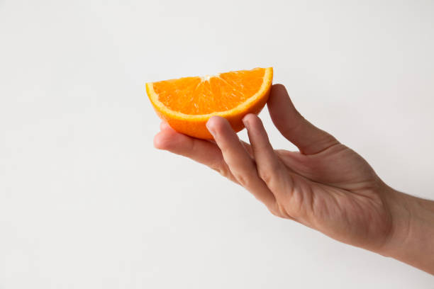 istock Person holding orange slice in fingers isolated on white 1221765562