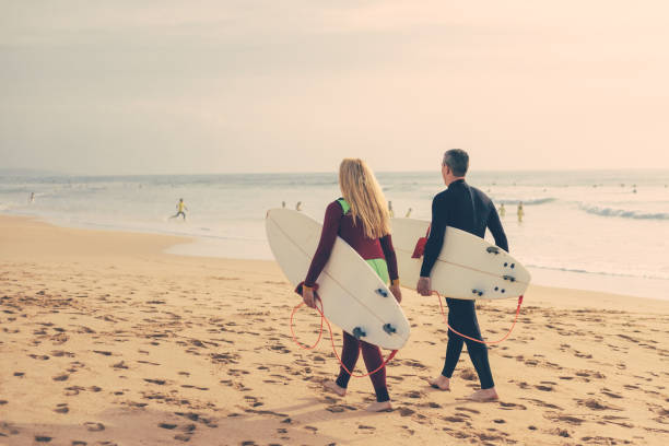 istock Back view of couple with surfboards walking on beach 1221768525