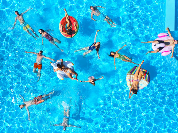 インフレータブルフラミンゴ、白鳥、マットレスとスイミングプールでパーティーをしている友人の空中。幸せな若者は晴れた日に高級リゾートでリラックスします。上から見る。太陽の下� - floating on water women swimming pool water ストックフォトと画像