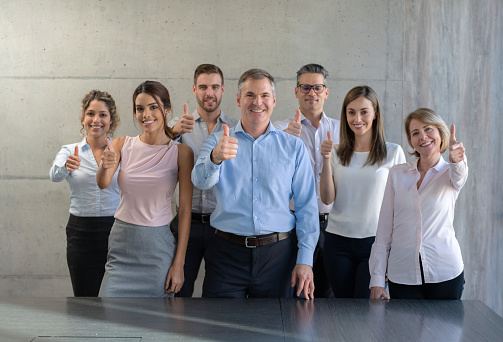 Portrait of a happy group of business people with thumbs up at the office