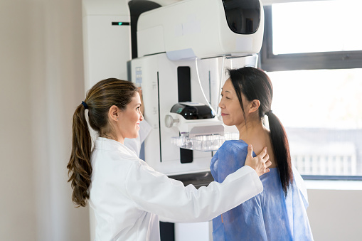 Médico femenino hablando con su paciente y ajustando su posición para hacer una mamografía photo