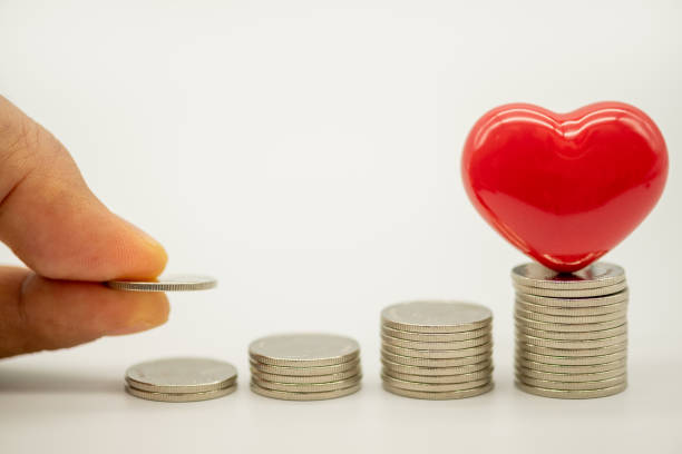 Money, Financial,Saving, Business Growth concept, Closeup of man hand put coin to coins stack and ceramic red heart on top of coins stack on white background and copy space for text. dinero, financiero, ahorro, concepto de crecimiento de negocio, primer plano de la mano del hombre poner moneda a la pila de monedas y corazón rojo de cerámica en la parte superior de las monedas pila sobre fondo blanco y copiar espacio para el texto.
