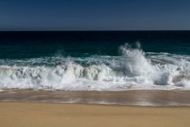 The ocean is calm and the beach is empty. The water is a beautiful shade of blue. The sand is dry and the beach is deserted