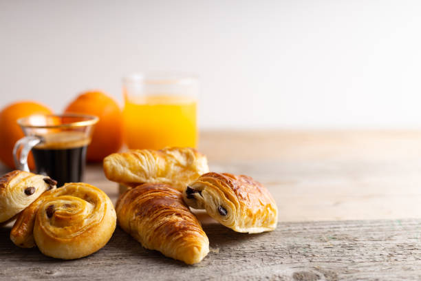 Breakfast with croissants, cinnamon buns and chocolate cookies, fresh orange juice and coffee on the side on a wooden background.