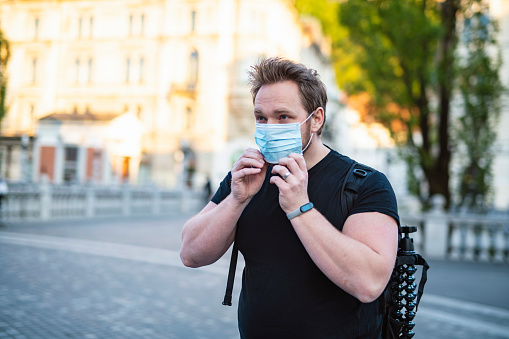 Caucasian Man Putting On Face Mask In The City To Prevent Getting Coronavirus, COVID-19