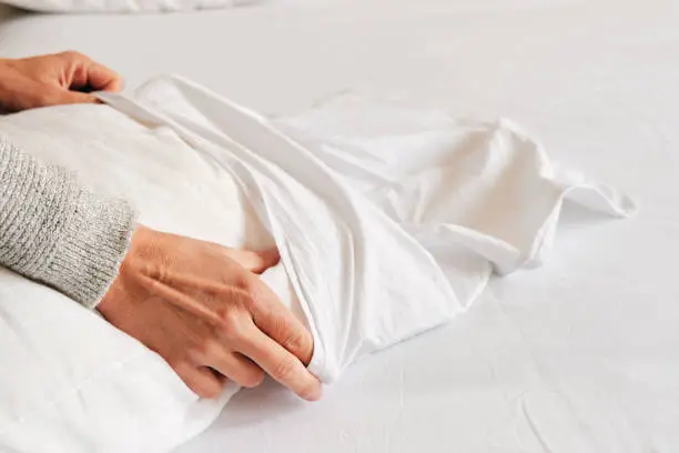 closeup of a young caucasian man introducing a pillow into a white pillow case as he is making the bed