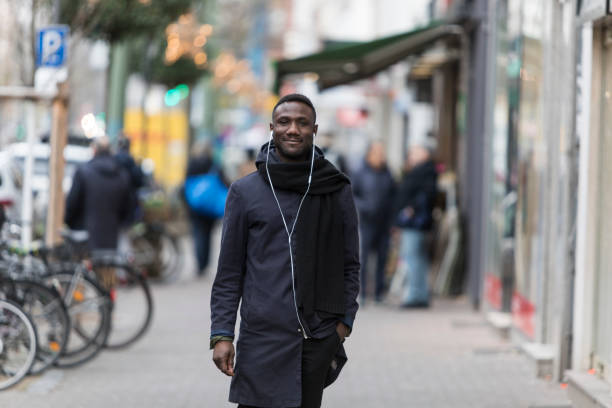 istock Handsome Black Man with Earphones and Hand in Pocket Posing on Sidewalk 1221782613