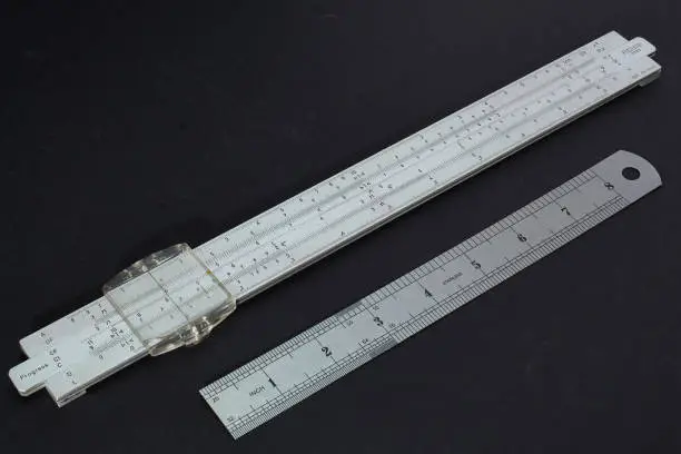 old slide rule made of metal from 1965 with a ruler for size comparison
