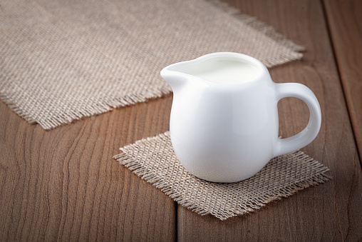 White jug with milk on a wooden rustic background.