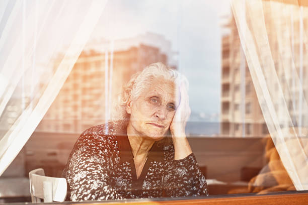 istock Elderly woman sitting alone and looking sadly outside the window 1221787916