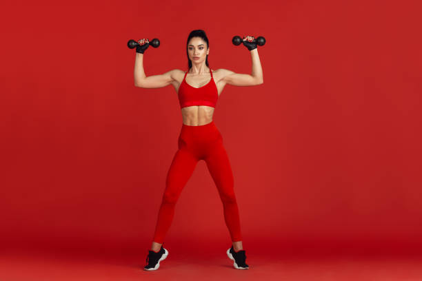 istock Beautiful young female athlete practicing on red studio background, monochrome portrait 1221789870