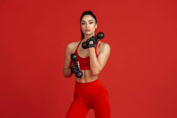 istock Beautiful young female athlete practicing on red studio background, monochrome portrait 1221789871