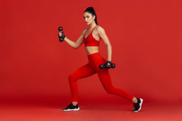 istock Beautiful young female athlete practicing on red studio background, monochrome portrait 1221789874