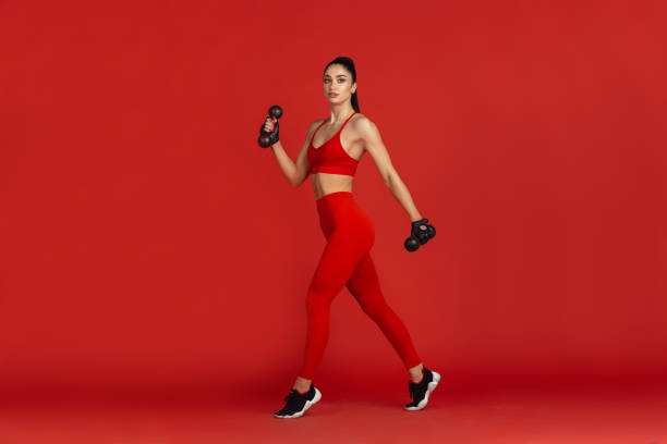 istock Beautiful young female athlete practicing on red studio background, monochrome portrait 1221789877