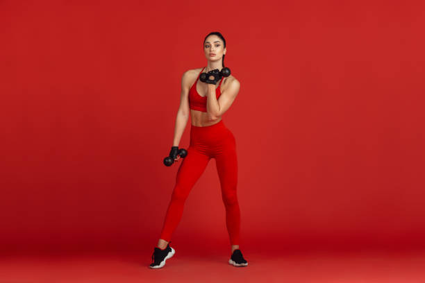 istock Beautiful young female athlete practicing on red studio background, monochrome portrait 1221789878
