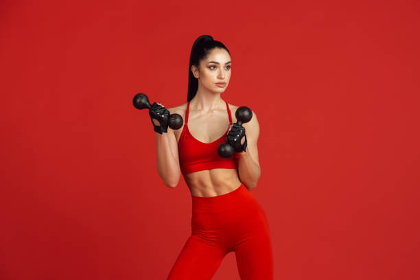 istock Beautiful young female athlete practicing on red studio background, monochrome portrait 1221789880