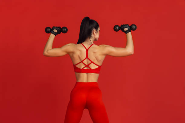 istock Beautiful young female athlete practicing on red studio background, monochrome portrait 1221789881