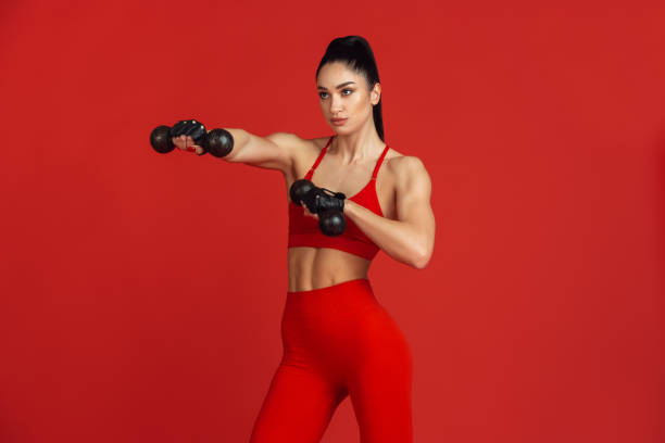 istock Beautiful young female athlete practicing on red studio background, monochrome portrait 1221789882