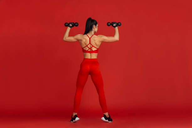 istock Beautiful young female athlete practicing on red studio background, monochrome portrait 1221789884