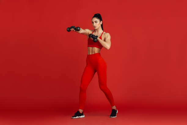 Beautiful young female athlete practicing on red studio background, monochrome portrait