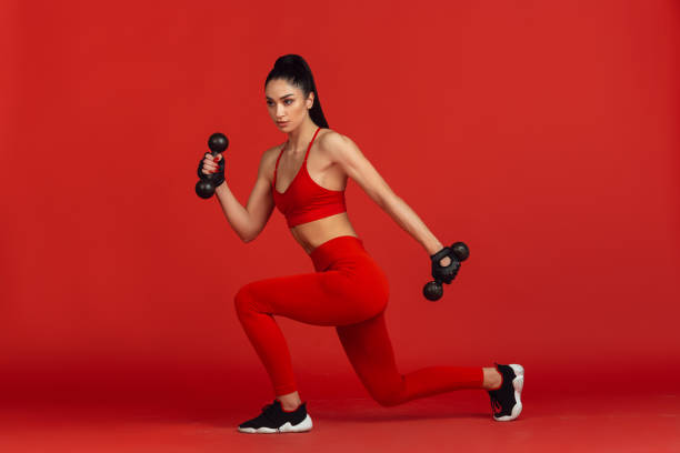 istock Beautiful young female athlete practicing on red studio background, monochrome portrait 1221789897