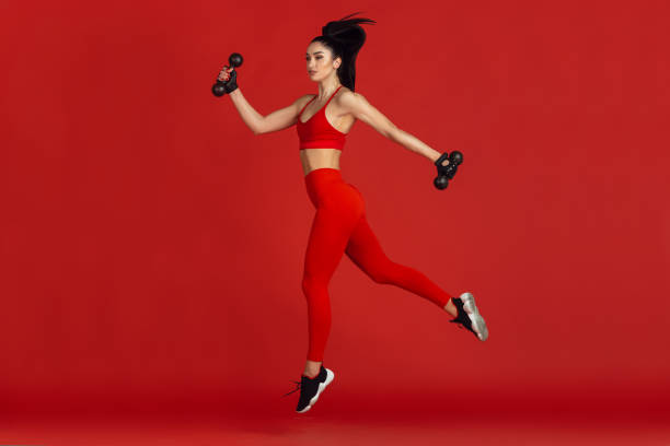istock Beautiful young female athlete practicing on red studio background, monochrome portrait 1221789898