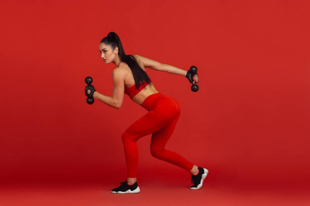 istock Beautiful young female athlete practicing on red studio background, monochrome portrait 1221789901