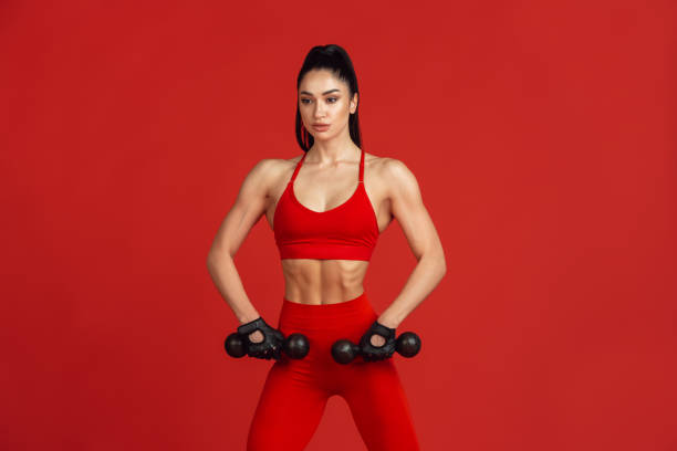 istock Beautiful young female athlete practicing on red studio background, monochrome portrait 1221789902
