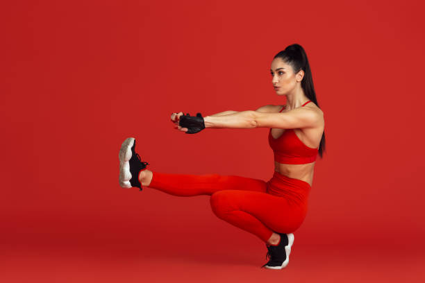 istock Beautiful young female athlete practicing on red studio background, monochrome portrait 1221789946