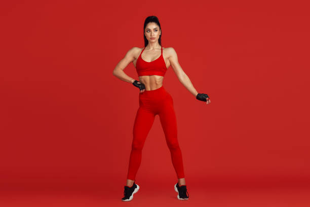 istock Beautiful young female athlete practicing on red studio background, monochrome portrait 1221789949