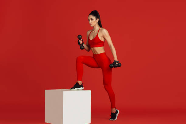 istock Beautiful young female athlete practicing on red studio background, monochrome portrait 1221789953