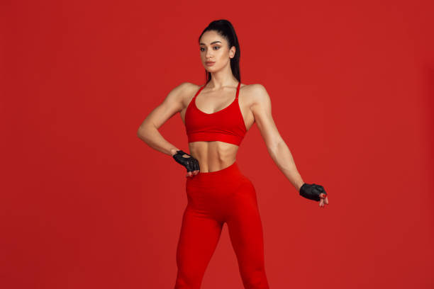 istock Beautiful young female athlete practicing on red studio background, monochrome portrait 1221789954