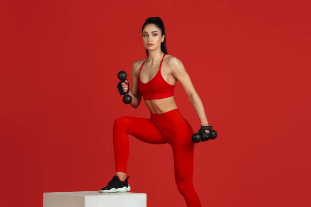 istock Beautiful young female athlete practicing on red studio background, monochrome portrait 1221789960