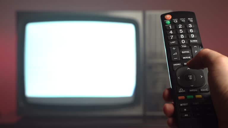 Old vintage television on auction market, close-up of man's hand holding remote control and pushing buttons for changing channels. Antique retro TV with blinking screen on dark red background, technologies of old-fashioned times