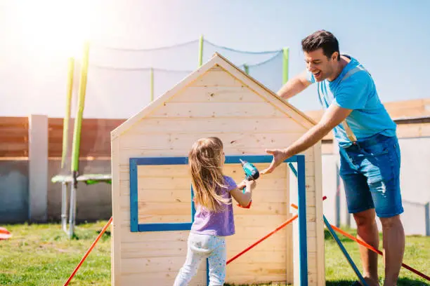 Father assembling wooden house for his daughter at home playground back yard