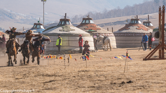 ULAANBAATAR, MONGOLIA - MARCH 5 2019 : Mongolian Archery people in tradition clothes on horseback riding and shooting arrow from at village Ger in Mongolia.