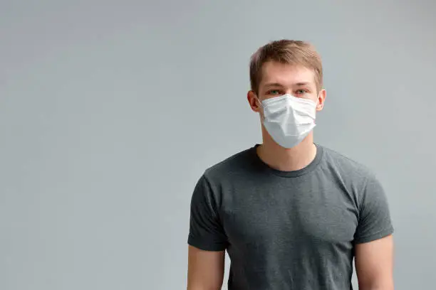 Cute boy in a medical mask, in a black t-shirt on a gray background. Poster about the quarantine and the pandemic