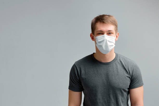 cute boy in a medical mask, in a black t-shirt on a gray background. poster about the quarantine and the pandemic. - pensive question mark teenager adversity imagens e fotografias de stock