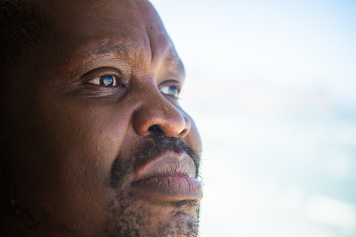 An African senior male close up of his face showing his facial hair, eyes and lips.  There is a reflection of the ocean in his eyes.