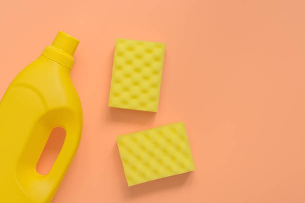 istock Flat lay yellow plastic bottle for liquid detergent, cleaning agent, antibacterial gel and washing sponge on pastel pink background. House cleaning concept. Top view. 1221797575
