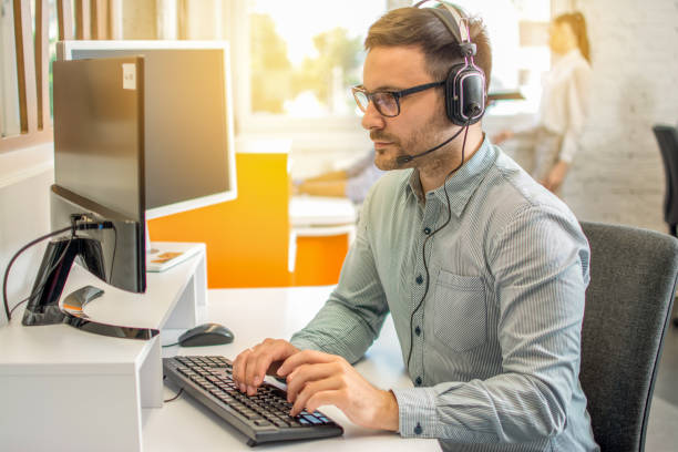 istock Male professional call center telesales agent wearing headset using computer in customer care support service office. 1221799964